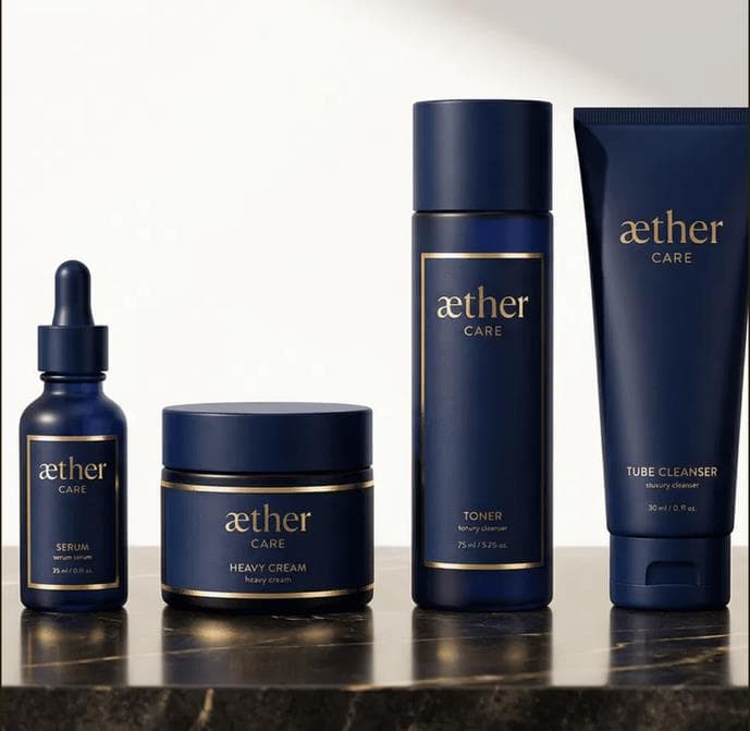 Línea AETHER CARE — serum, heavy cream, toner y tube cleanser en botellas navy con foil dorado sobre mármol